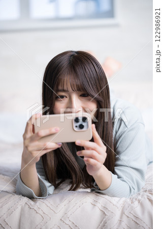 スマホを持って動画などを見るベッドで寝転ぶ笑顔の女性 スマホを持って動画などを見るベッドで寝転ぶ笑顔の女性 122986921