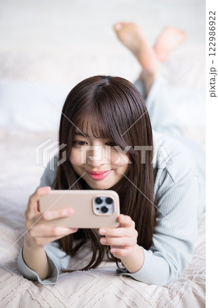 スマホを持って動画などを見るベッドで寝転ぶ笑顔の女性 スマホを持って動画などを見るベッドで寝転ぶ笑顔の女性 122986922