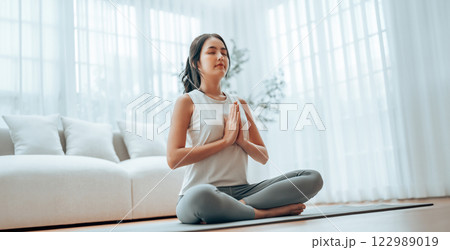 Young Asian woman meditating in lotus position at home Young Asian woman meditating in lotus position at home 122989019