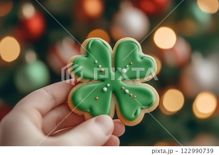 Green Shamrock Sugar Cookie with Icing Held Against Blurred Holiday Background 122990739