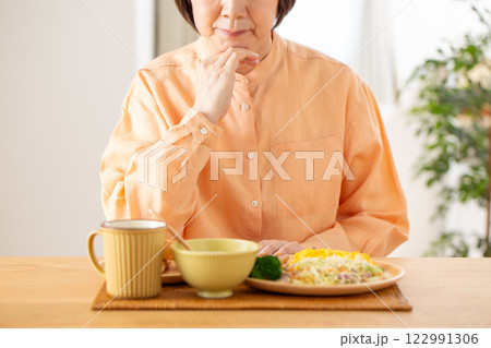 洋食の朝食を前に悩むミドル女性 122991306