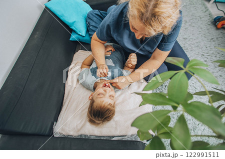 smiling boy lying on a soft blanket during a therapy session with a female specialist in a cozy room, concept of relaxation, childhood therapy, and healthcare smiling boy lying on a soft blanket during a therapy session with a female specialist in a cozy room, concept of relaxation, childhood therapy, and healthcare 122991511