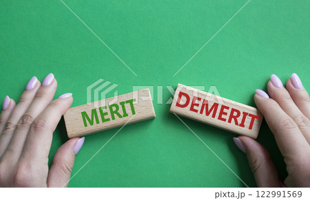 Merit or Demerit symbol. Concept word Merit or Demerit on wooden blocks. Businessman hand. Beautiful green background. Business and Merit or Demerit concept. Copy space 122991569