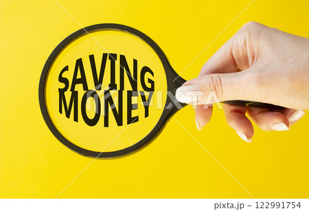 Saving Money symbol. Concept words Saving Money on magnifying glass. Businessman hand. Beautiful yellow background. Business and Saving Money concept. Copy space. 122991754