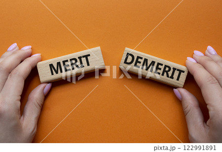 Merit or Demerit symbol. Concept word Merit or Demerit on wooden blocks. Businessman hand. Beautiful orange background. Business and Merit or Demerit concept. Copy space 122991891
