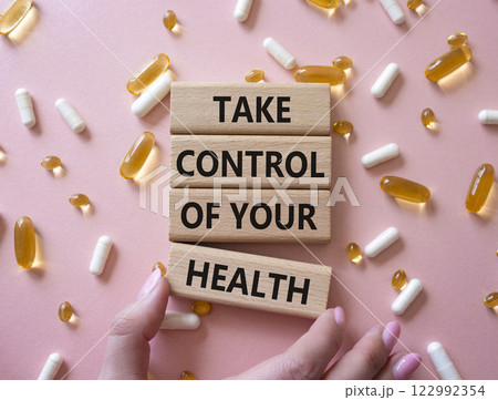 Health symbol. Concept word Take Control of your Health on wooden blocks. Businessman hand. Beautiful pink background with pills. Medicine concept. Copy space Health symbol. Concept word Take Control of your Health on wooden blocks. Businessman hand. Beautiful pink background with pills. Medicine concept. Copy space 122992354