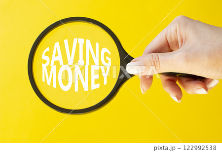 Saving Money symbol. Concept words Saving Money on magnifying glass. Businessman hand. Beautiful yellow background. Business and Saving Money concept. Copy space. Saving Money symbol. Concept words Saving Money on magnifying glass. Businessman hand. Beautiful yellow background. Business and Saving Money concept. Copy space. 122992538