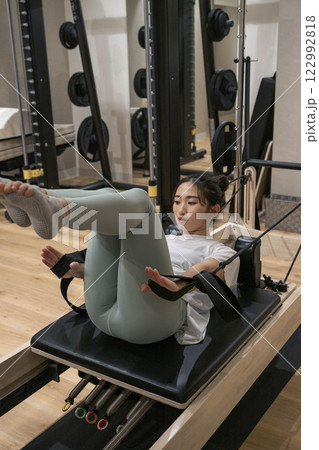室内のジムでマシンピラティスをする若い女性 室内のジムでマシンピラティスをする若い女性 122992818