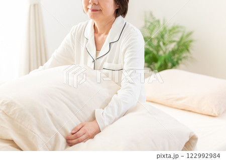 朝の寝室で微笑む白いパジャマ姿のミドル女性 朝の寝室で微笑む白いパジャマ姿のミドル女性 122992984