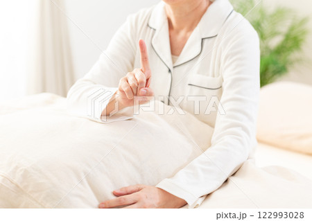 朝の寝室で人差し指を立てる白いパジャマ姿のミドル女性 朝の寝室で人差し指を立てる白いパジャマ姿のミドル女性 122993028