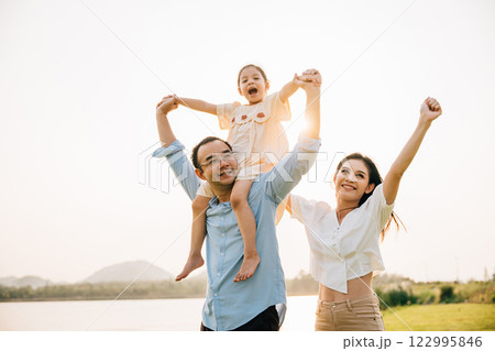 Asian family child girl piggyback riding back on father raising hands like flying outdoor nature park with mother, Happy parent daughter having fun together, Tourist lifestyle family leisure activity 122995846