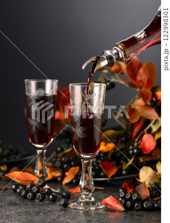 Black chokeberry drink is poured from a bottle into a glass. 122998301