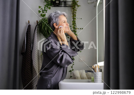 Mature happy aged beautiful woman during menopause with grey hair applying makeup on her face Mature happy aged beautiful woman during menopause with grey hair applying makeup on her face 122998679