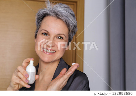 Beautiful elderly woman pensioner during menopause with gray hair applies hormonal anti-aging cream Beautiful elderly woman pensioner during menopause with gray hair applies hormonal anti-aging cream 122998680
