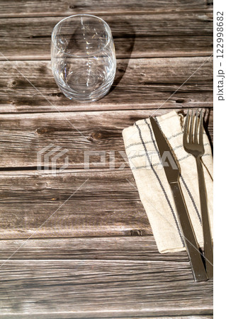 knife, fork and a transparent glass on top of a wooden table knife, fork and a transparent glass on top of a wooden table 122998682