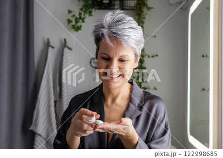 Mature beautiful woman during menopause with gray hair applies hormonal anti-aging cream Mature beautiful woman during menopause with gray hair applies hormonal anti-aging cream 122998685