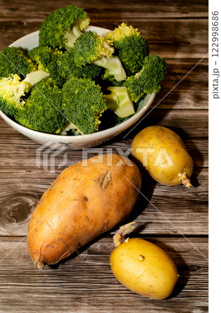 Bowl of broccoli, sweet potato and raw potatoes on a wooden table Bowl of broccoli, sweet potato and raw potatoes on a wooden table 122998686