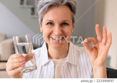 A beautiful elderly woman pensioner with gray hair holds a pink round contraceptive hormonal pill A beautiful elderly woman pensioner with gray hair holds a pink round contraceptive hormonal pill 122998697