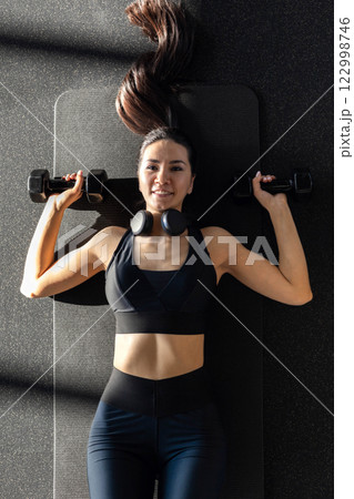 Strong beautiful fitness woman training back doing exercise with dumbbells at gym. 122998746