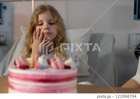 A joyful child is celebrating a special birthday with a delightful cake in a hospital room 122998784