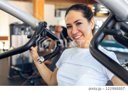 Portrait smiling sport woman exercising on a strength training machine for arms posing 122998807