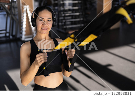 Young beautiful Asian woman doing fitness exercises on the TRX machine in the gym. Young beautiful Asian woman doing fitness exercises on the TRX machine in the gym. 122998831