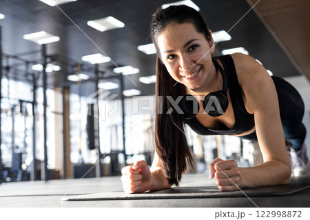 Smiling fitness woman stand in plank position doing push ups training at gym. Smiling fitness woman stand in plank position doing push ups training at gym. 122998872