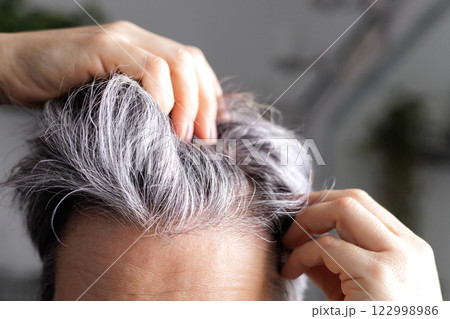 An adult woman of age with gray hair examines in front of the mirror the amount of gray hair on head 122998986