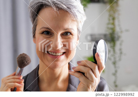 Beautiful smiling elderly woman pensioner during menopause with gray hair applies anti-aging makeup 122998992