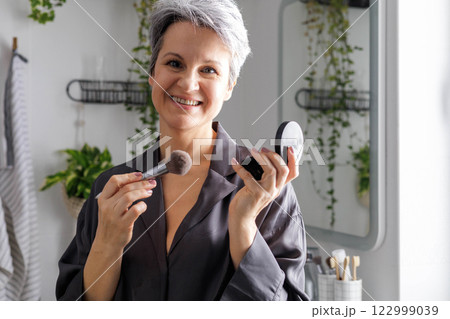 Beautiful smiling elderly woman pensioner during menopause with gray hair applies anti-aging makeup 122999039