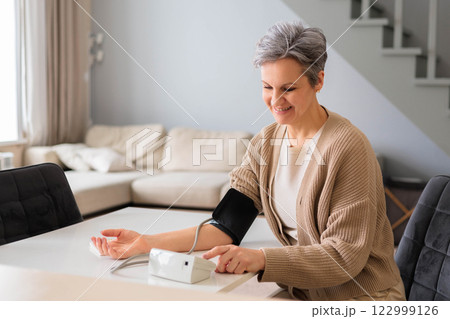 An elderly beautiful woman in old age with gray hair measures blood pressure with tonometer. An elderly beautiful woman in old age with gray hair measures blood pressure with tonometer. 122999126