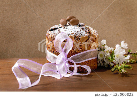 Homemade Italian traditional Easter panettone cake, decorated by chocolate eggs, pink ribbon and blossoming cherry tree flowers standing on wooden table. Traditional Easter European bake. Copy space Homemade Italian traditional Easter panettone cake, decorated by chocolate eggs, pink ribbon and blossoming cherry tree flowers standing on wooden table. Traditional Easter European bake. Copy space 123000822