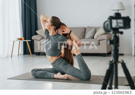 Doing lessons on camera. Young woman with slim body type and in yoga clothes is at home 123002963