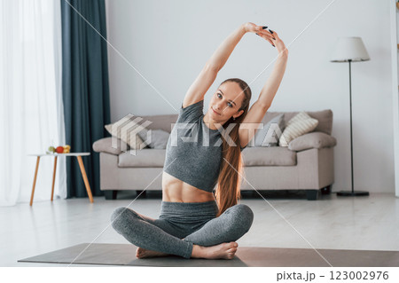 Sitting on the floor. Young woman with slim body type and in yoga clothes is at home 123002976