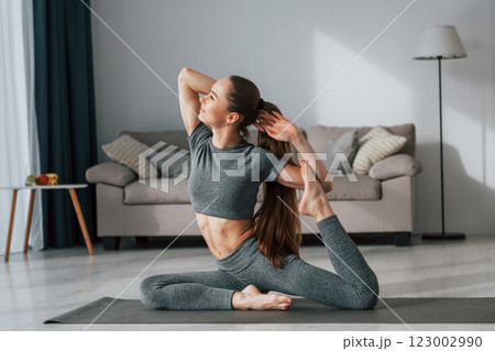 Stretching the legs. Young woman with slim body type and in yoga clothes is at home 123002990