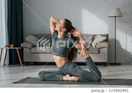 Stretching the legs. Young woman with slim body type and in yoga clothes is at home 123002991