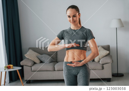 Standing in domestic room. Young woman with slim body type and in yoga clothes is at home 123003038
