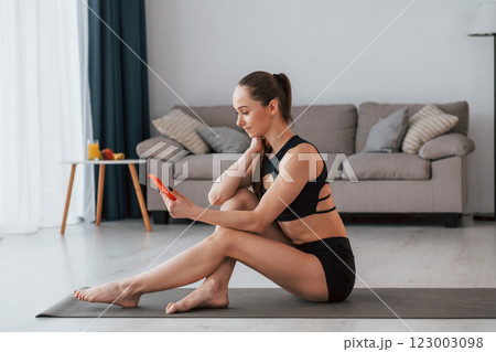 With phone in hands. Young woman with slim body type and in yoga clothes is at home 123003098