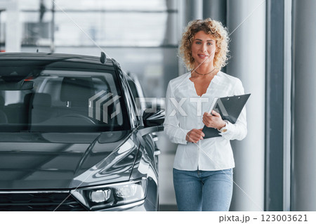 Holding notepad. Woman with curly blonde hair is in autosalon Holding notepad. Woman with curly blonde hair is in autosalon 123003621