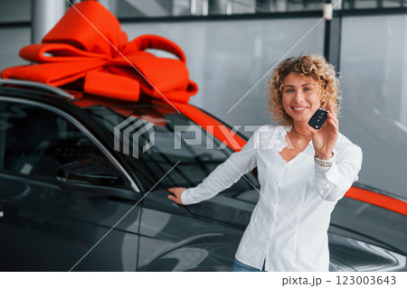 Car is with gift length on the top. Woman with curly blonde hair is in autosalon Car is with gift length on the top. Woman with curly blonde hair is in autosalon 123003643