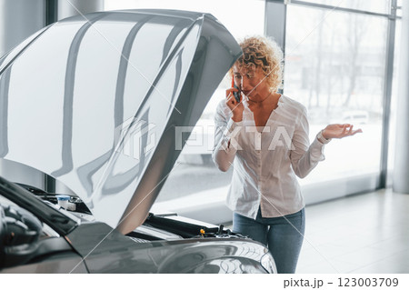 Car is damaged, hood is opened. Woman with curly blonde hair is in autosalon 123003709
