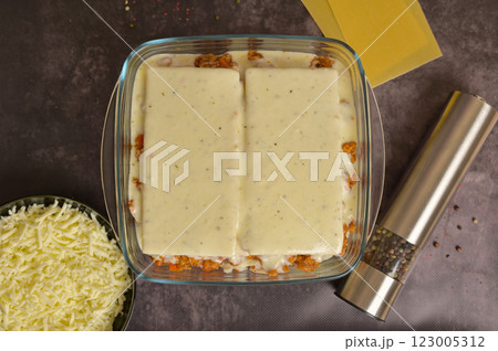 Top view. Homemade lasagna cooking preparation. Lasagne pasta sheets, Bolognese sauce in a glass form. Grated cheese in a black bowl, pepper mill. Black background Top view. Homemade lasagna cooking preparation. Lasagne pasta sheets, Bolognese sauce in a glass form. Grated cheese in a black bowl, pepper mill. Black background 123005312