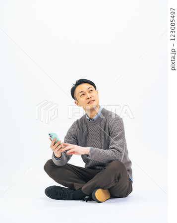 座ってスマホを使うカジュアルウェアのミドル男性の全身写真 123005497
