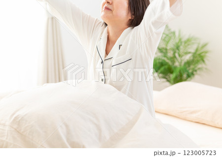 朝の寝室で伸びをする白いパジャマ姿のミドル女性 123005723