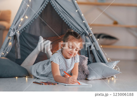 With writing equipment. Cute little girl playing in the tent that is in the domestic room 123006188