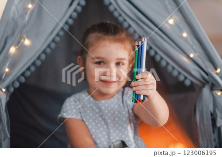 Holding pencils. Cute little girl playing in the tent that is in the domestic room 123006195