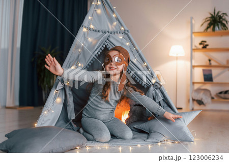 In pilot glasses. Cute little girl playing in the tent that is in the domestic room In pilot glasses. Cute little girl playing in the tent that is in the domestic room 123006234