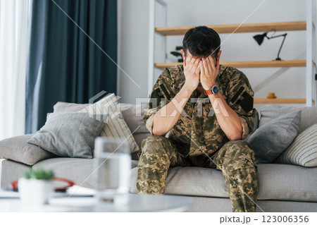 Having flashbacks. Post traumatic stress disorder. Soldier in uniform sitting indoors 123006356