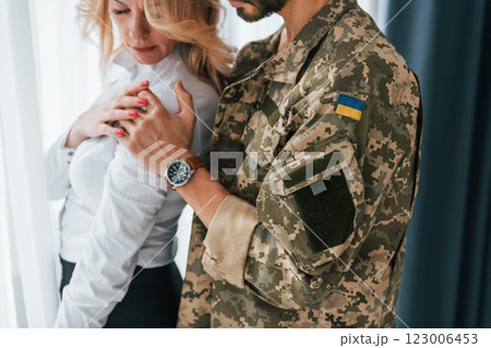 Flag of Ukraine. Soldier with his wife standing indoors and embracing Flag of Ukraine. Soldier with his wife standing indoors and embracing 123006453