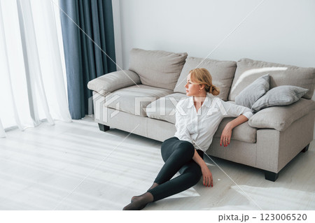 In black jeans. Woman in formal wear sitting on the floor near sofa in domestic room 123006520